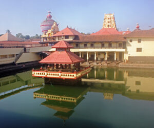 Holy Shrine dedicated to Hindu Deity, Lord Krishna. Picture taken in the town of Udupi, in the state of Karnataka, South India.   Picture shot on Feb 10, 2014, and shows the holy tank in the foreground, with the Temple towers seen in the background.  The building in the center of the tank, known as Mandapam, is where the sacred rituals are carried out. Four pillared corridors surround the tank with steps descending to the water.  This is for the convenience of devotees to take a dip in the holy tank, before entering the Temple. The holy tank here is named Madhava Sarovar, after the local saint Madhavacharya, who preached a form of Hinduism, several centuries ago.